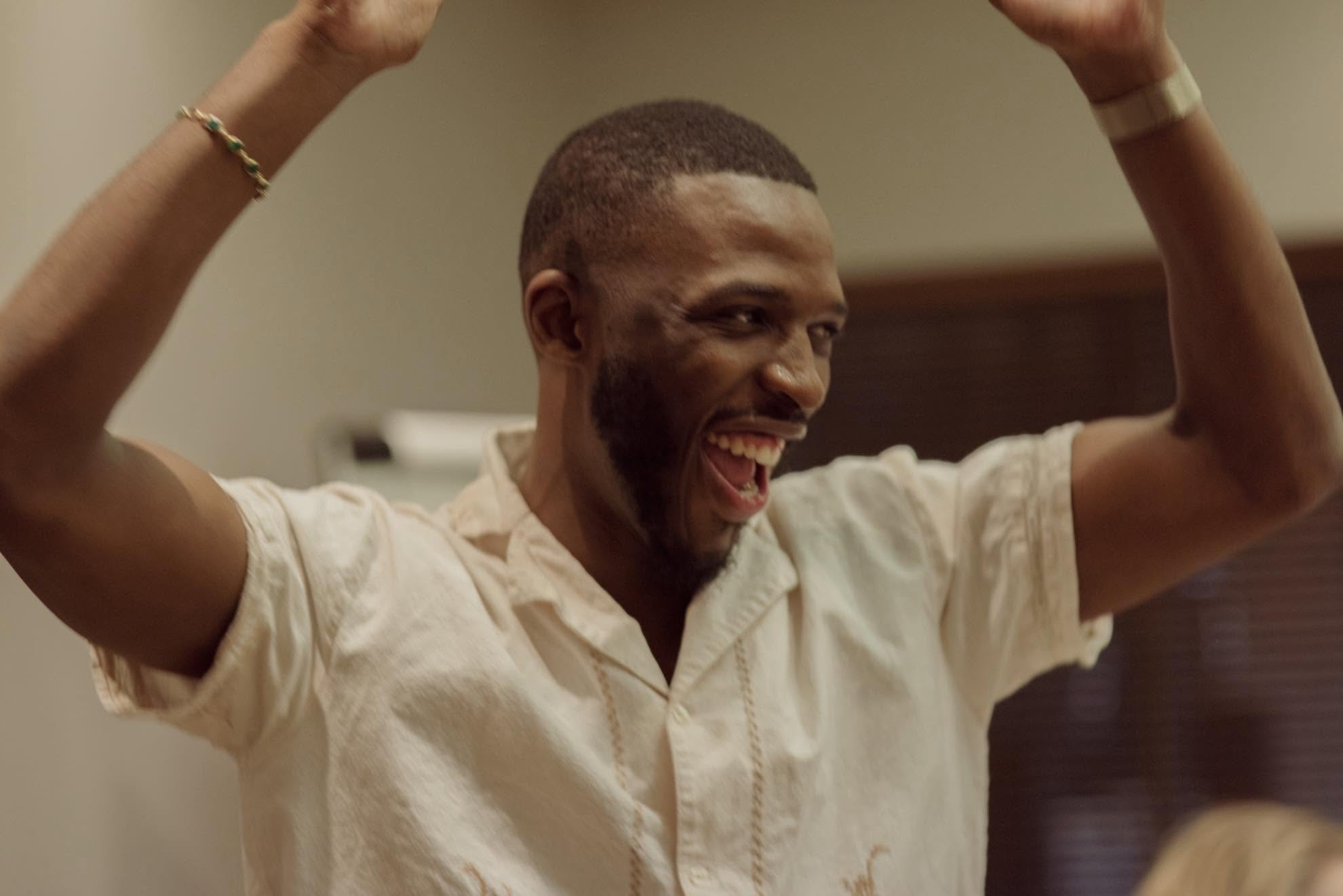 Washington laughing, both arms raised, in a workshop room